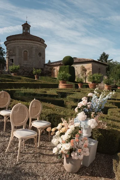Ceremony setup featuring garden ceremony decor and lush floral arrangements, framed by formal hedges before a historic stone building.
