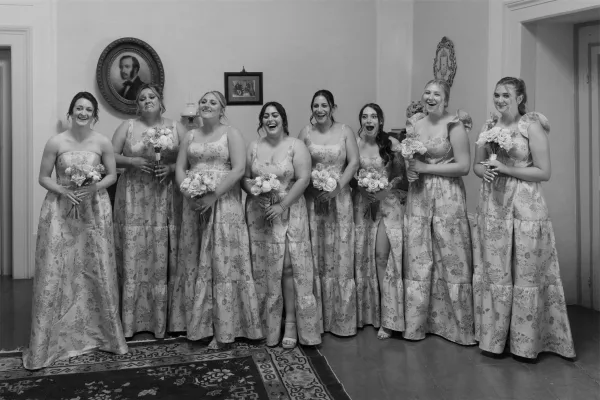 Bridesmaids portrait in matching bridesmaid dresses, standing with bouquets in an elegant interior with framed artwork.