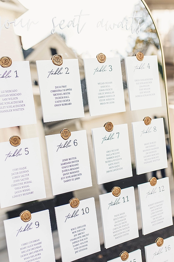 Wedding seating chart mirror seating chart with calligraphy escort cards and wax seals arranged on a black-framed mirror on a sunlit patio