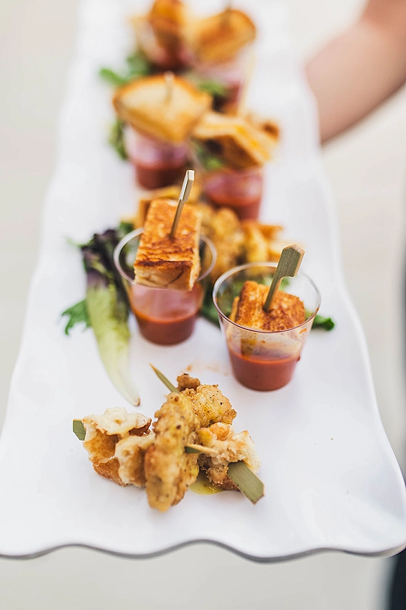 Wedding cocktail appetizers on a platter with skewers and mini cups, dipping sauce, and lettuce garnish held by a server hand