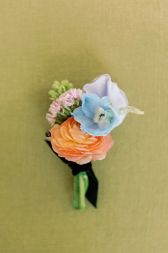 Wedding boutonniere featuring ranunculus and a white calla lily with greenery and ribbon wrap on a green fabric backdrop
