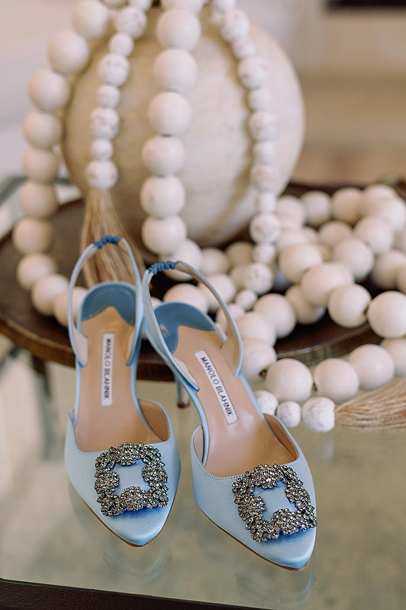Bridal shoes in blue wedding shoes style, satin slingback heels with crystal buckle clips on a glass tabletop with beaded garland accents