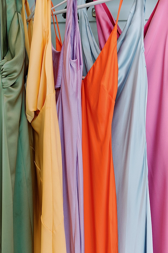 Bridesmaid dresses in a colorful bridesmaid dress color palette, satin slip styles with spaghetti straps on hangers by a closet door