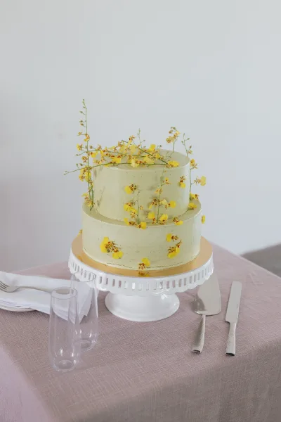 Wedding cake, a two tier wedding cake in smooth buttercream adorned with fresh flowers, displayed on a mauve tablecloth.