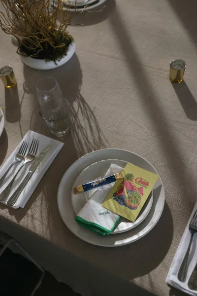 Wedding place setting on a neutral linen table setting, with an embroidered napkin, bathed in soft sunlight shadows.