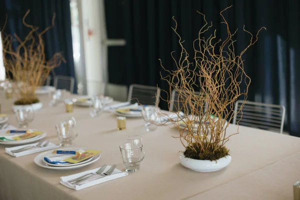 Reception tablescape featuring a modern branch centerpiece of curly willow, styled in a neutral palette along a minimalist long banquet table