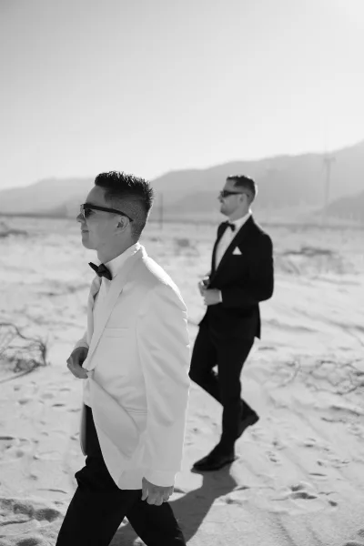 Groom portrait featuring a groom with a classic bow tie, set amid desert sand with mountains and wind turbines beneath a clear sky.