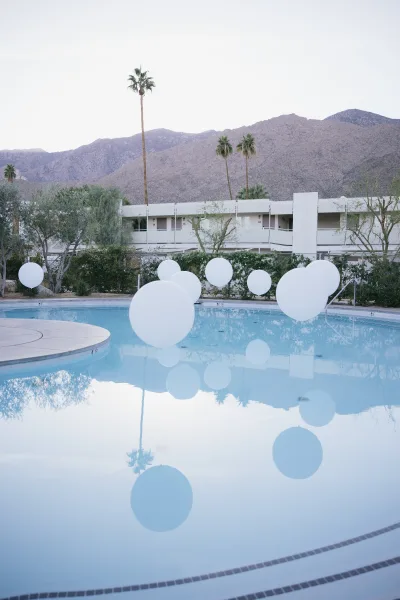 Poolside wedding decor with floating balloon decor, white balloons drifting over the hotel swimming pool with palm trees and mountains beyond