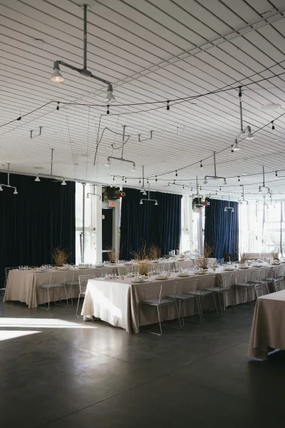 Reception tablescape in minimalist reception decor featuring dried branch centerpieces, framed by blue velvet curtains and large windows.
