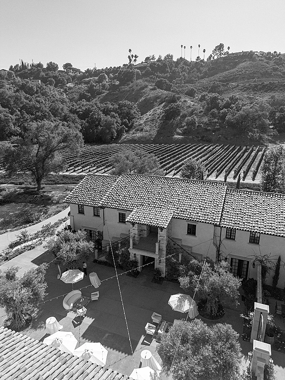 Wedding venue aerial view of a vineyard wedding venue courtyard with string lights, umbrellas, cocktail tables, and lounge seating amid hillside rows
