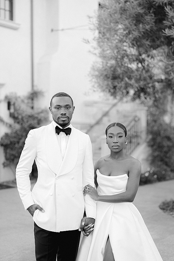 Couple portrait in a black and white wedding portrait, bride and groom holding hands on an outdoor walkway by stairs and trees