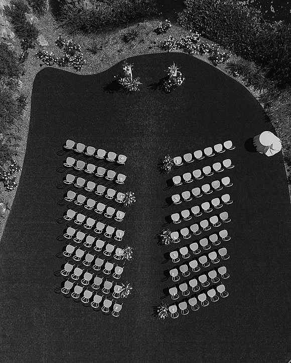Ceremony setup with outdoor ceremony seating of white chairs in two rows facing a floral arch on a manicured garden lawn