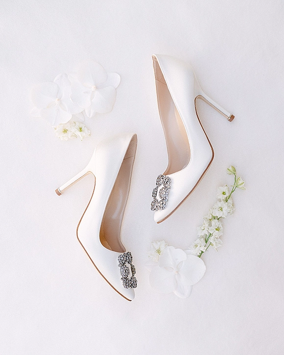 Wedding shoes in a bridal heels flat lay with crystal buckle white high heels styled with white orchids on a clean white backdrop