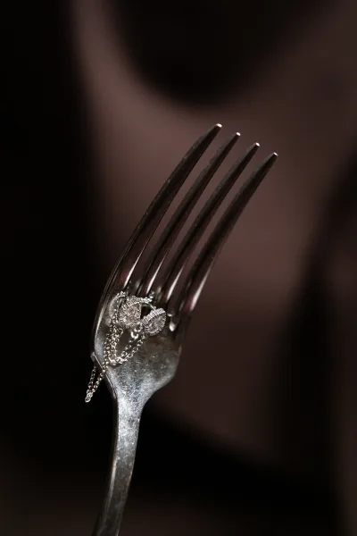 Wedding rings wedding ring flatlay balanced on a fork beside a delicate jewelry chain, diamond sparkle against a moody dark blurred background