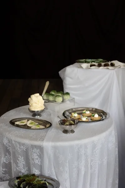Wedding dessert table dessert table setup with silver serving trays and bite-size sweets on white linens, set against black drapery backdrop