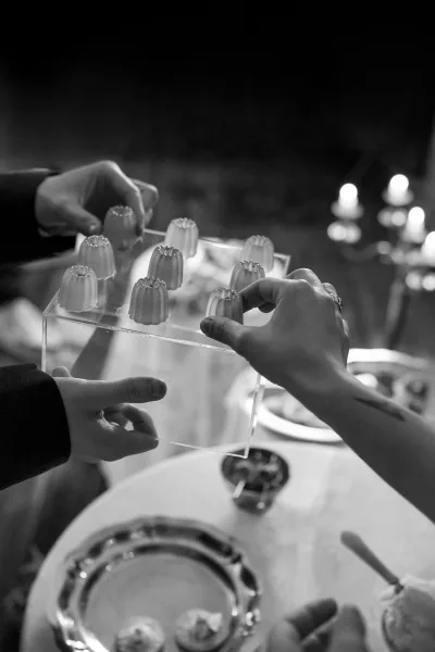 Wedding dessert serving with a mini dessert tray on a clear acrylic platter beside silver charger, cutlery, and candlelit reception table bokeh