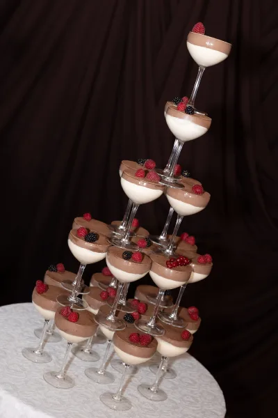 Dessert tower wedding dessert table with martini glass mousse cups topped with raspberries and currants against a dark draped backdrop