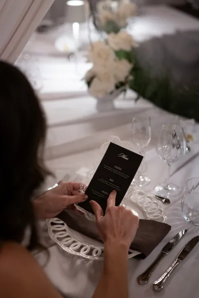 Wedding menu card in a formal place setting, black lace-edge menu on white plate with napkin, glassware, and centerpiece on a long banquet table