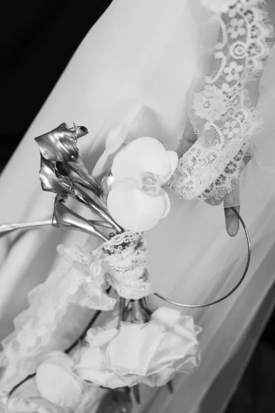 Bridal bouquet with white orchid bouquet and metallic calla lilies, wrapped in lace and ribbon, resting on wedding dress fabric