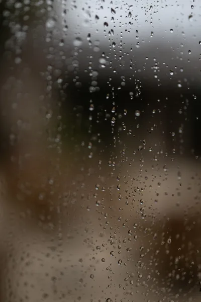 Rainy wedding photo of a couple seen through window glass with raindrops, creating a moody wedding rain photography feel and blurred outdoors