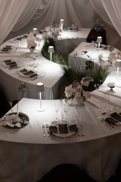 Reception tablescape with white wedding table decor, floral and greenery centerpieces, and a portable lamp under a draped fabric canopy