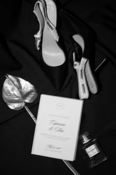 Invitation suite wedding invitation flat lay with black and white cards, bridal slingback heels and perfume on black fabric backdrop