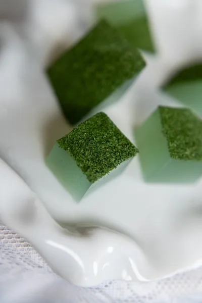 Wedding favor boxes with moss wedding favors in a white ceramic dish, styled with green boxes on a lace tablecloth on white surface