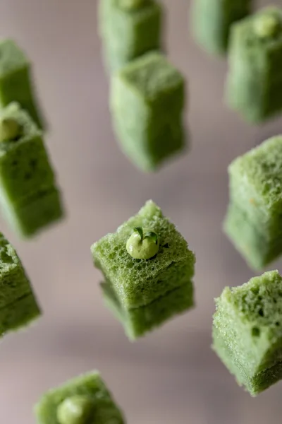 Wedding dessert bites of mini dessert cubes with green sponge cake, piped frosting, and microgreens garnish on a neutral tabletop