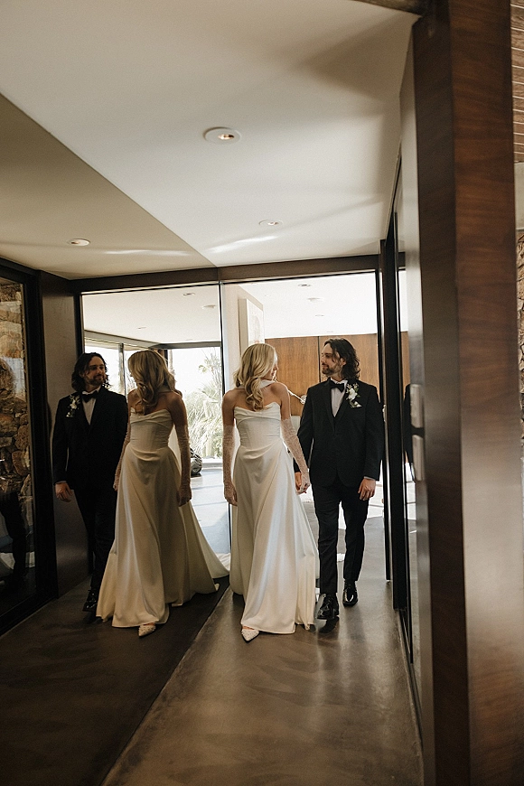 Couple portrait of bride and groom walking in a modern hallway, bride in strapless dress with lace gloves, mirrored wall reflection behind