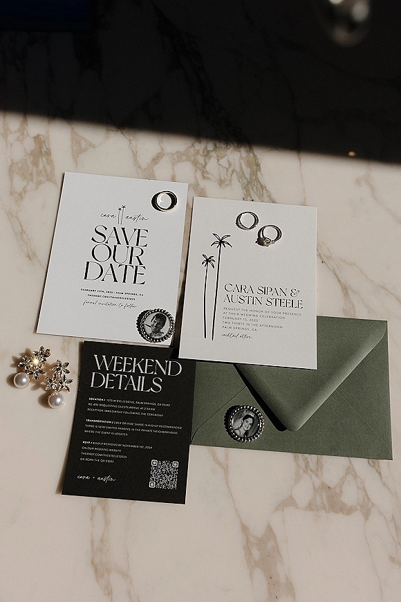 Wedding invitation suite with save the date card, rings and stud earrings in a flat lay on marble, featuring a QR code and envelope liner