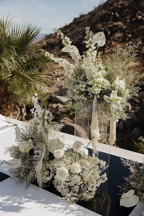 Wedding ceremony flowers in white roses and anthurium on an acrylic plinth with aisle florals, set against rocky desert hills and sky