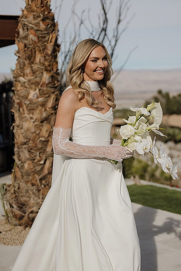 Bridal portrait of a bride in a strapless wedding dress holding a white calla lily bouquet, posed by palm trees in a desert landscape
