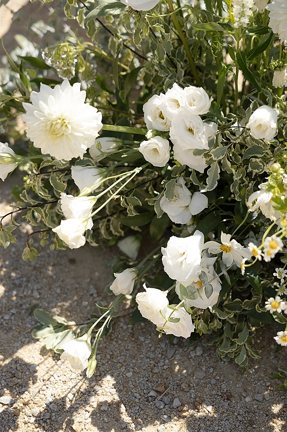Wedding flowers with white wedding flowers and variegated greenery arranged on sunlit gravel, casting soft shadows in close-up