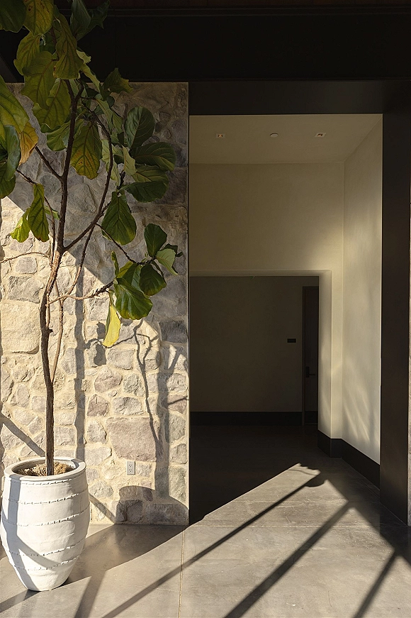 Wedding venue entrance with a potted tree in a large planter, framed by a stone wall and tiled hallway with long shadows