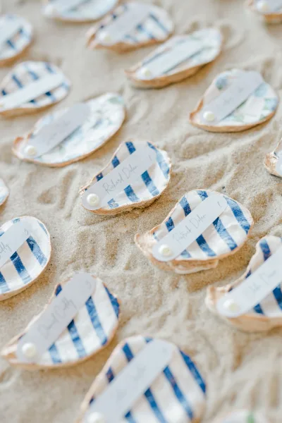 Wedding place cards on oyster shells with calligraphy name tags and pearl accents arranged on sand for a coastal table display