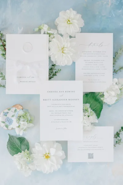 Invitation suite wedding invitation flat lay with RSVP and details cards beside a wax seal envelope, hydrangea blooms on blue watercolor surface