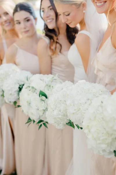 Bride with bridesmaids in a bridesmaid group portrait, holding white hydrangea bouquets with greenery in a light, airy outdoor setting