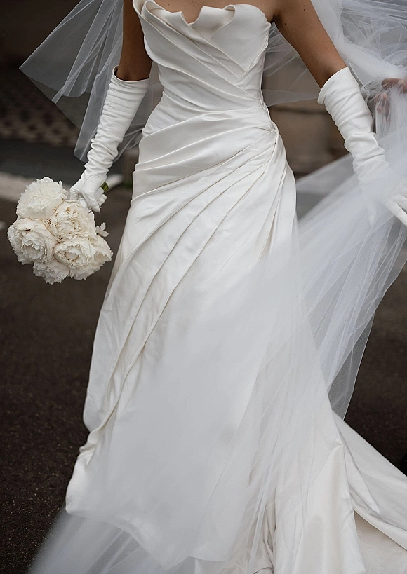 Wedding dress close-up of a strapless draped wedding dress with long gloves and a white bouquet on stone steps outdoors