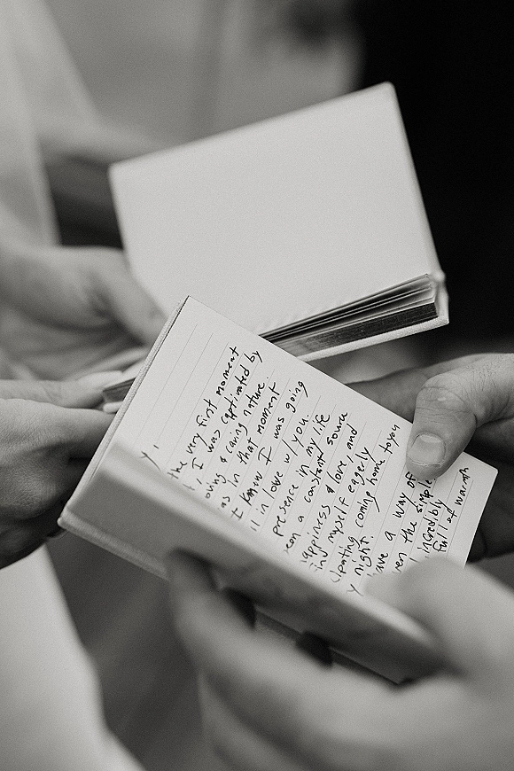 Wedding vows in a handwritten vow booklet held in both hands, captured close up with a softly blurred indoor background