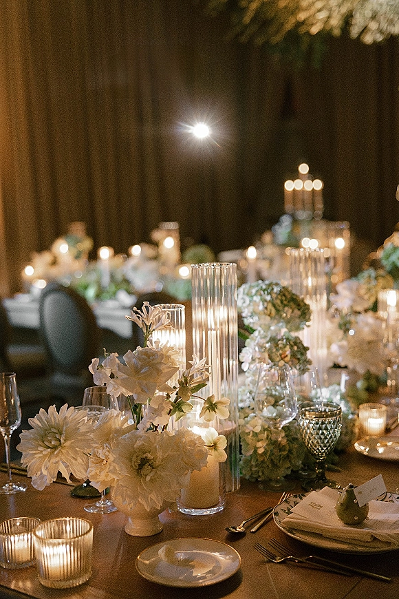 Reception tablescape with candlelit wedding reception glow, white florals and greenery, taper and pillar candles under bistro lights at night
