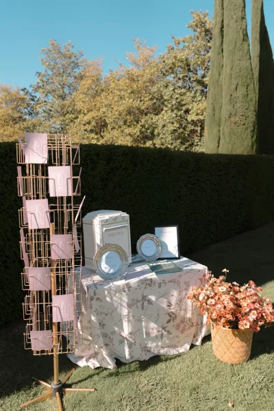 Guestbook table with a vintage mailbox guestbook, styled outdoors against a hedge wall and cypress trees on a lawn beneath a blue sky.