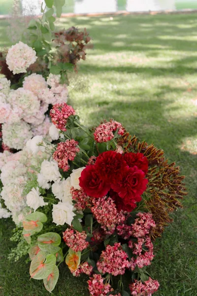 Wedding floral arrangement as a ground floral installation with red peonies on a grass lawn by a pond under tree shadows