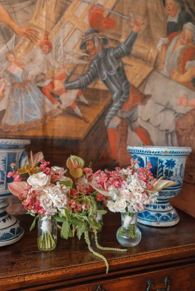 Bud vase centerpieces styled as entry table flowers with blue and white pottery on a wood dresser beneath a tapestry mural.