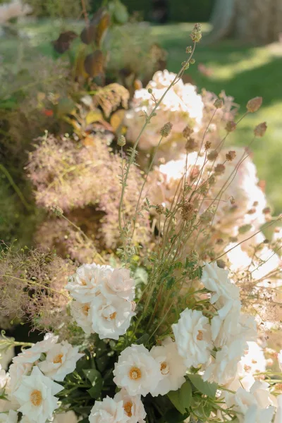 Wedding flowers in a white rose arrangement layered with airy grasses, styled in a meadow-like design.
