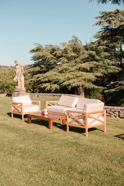 Wedding lounge setup for an outdoor wedding lounge by a stone wall and garden statue, arranged on the lawn with a bouquet accenting the seating area.