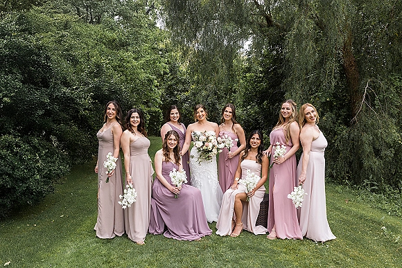 Bridesmaid group photo with bride and bridesmaids holding white flower bouquets on a garden lawn with trees and lush greenery