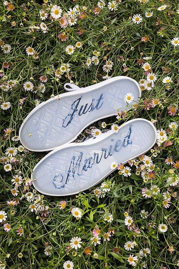Wedding shoes with custom wedding sneakers featuring clear rubber soles and lettering, styled in grass among wildflowers