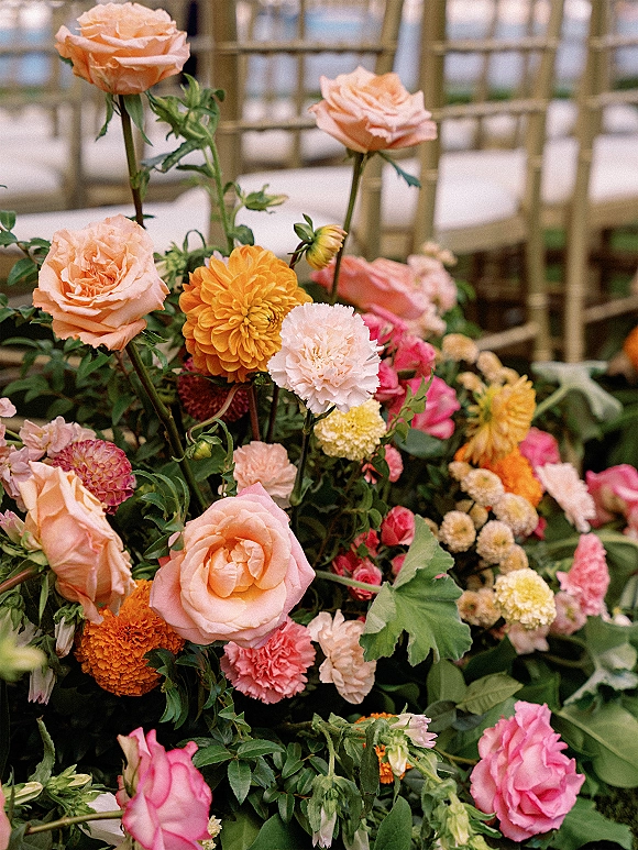 Wedding floral arrangement of roses and dahlias with greenery, set low on the floor beside gold Chiavari chairs indoors