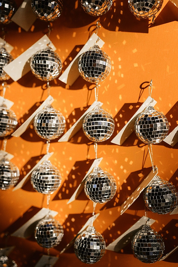 Disco ball decor with hanging disco balls on strings, paper tags and metal hooks, shimmering against an orange wall with shadows