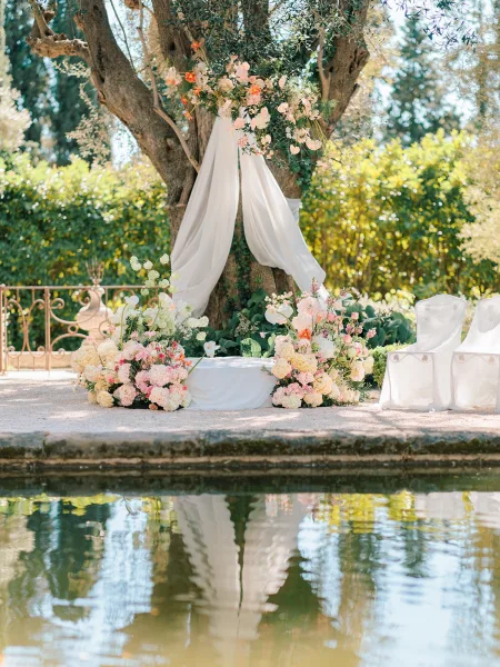 Ceremony altar decor with outdoor wedding altar on a white platform, floral arch and draped fabric by a pondside garden setting